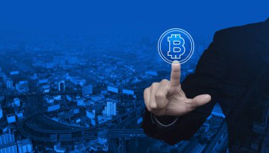İş adamı Bitcoin simgesini modern şehir kulesi, sokak, ekspres yol ve gökdelen üzerine bastırıyor, bitcoin konseptini seçiyor