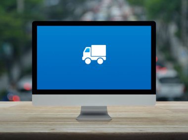 Masaüstü modern bilgisayar monitörü ekranındaki kargo kamyonu düz simgesi yoğun saatlerde ahşap masa üzerinde arabalar ve yollar, iş ulaşımı çevrimiçi servis kavramı