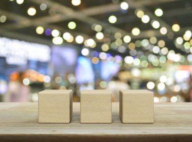 Bulanık ışığın ve alışveriş merkezinin gölgesinin üzerindeki ahşap masanın üzerinde üç tahta blok küp.