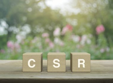 Tahta küpler üzerine CSR harfi. Bulanık pembe çiçek ve parktaki ağaç üzerine. Kurumsal Sosyal Sorumluluk kavramı.