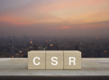 Tahta küpler üzerine CSR harfi sıcak gün batımında şehir manzarasının bulanıklığı üzerine kurulmuş sosyal sorumluluk kavramı.
