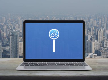 Seo simgesi dizüstü bilgisayar ekranında ahşap masa üzerinde şehir kulesi ve gökdelen üzerinde arama motoru optimizasyon konsepti