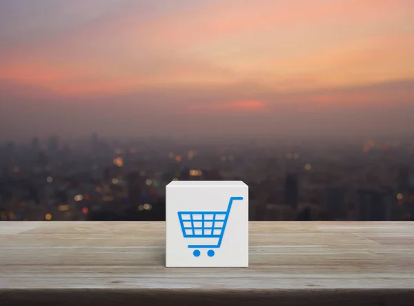 Shop cart icon on white block cube on wooden table over blur of cityscape on warm light sundown, Business shopping online concept