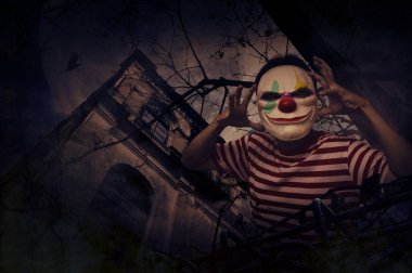 Korkunç kötü palyaço grunge kalesinin başında duruyor, ölü ağaç, kuş sineği, dolunay ve bulutlu gökyüzü, Cadılar Bayramı gizemi