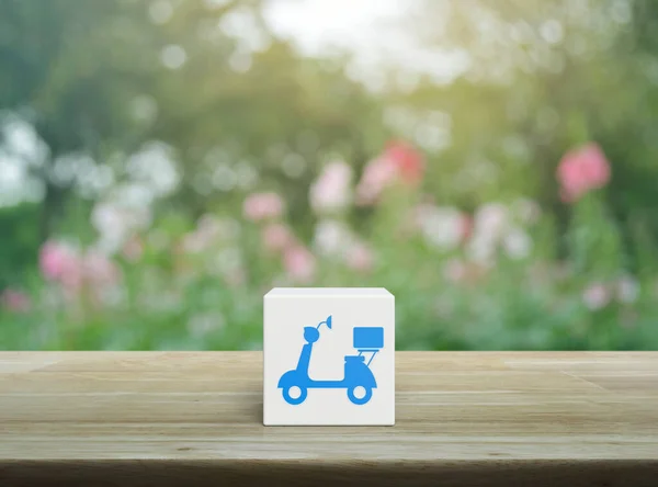 Motorcycle icon on white block cube on wooden table over blur pink flower and tree in garden, Business delivery service concept