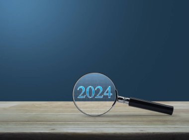 Açık mavi duvarın üzerindeki ahşap masa üzerinde 2024 yazılı metin ve mali grafiği olan büyüteç 2024 yılının mutlu yeni yılı araştırma konsepti