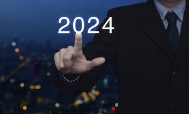 İş adamı 2024 'e basıyor. Bulanık renkli gece lambası modern şehir kulesi ve gökdelen üzerine. Yeni yılın kutlu olsun kapak konsepti.