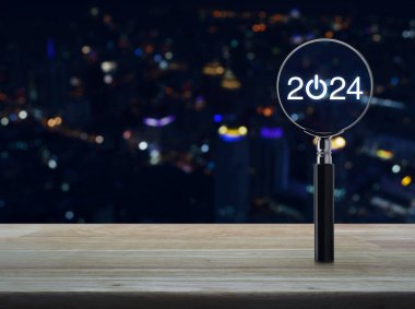 2024 tahta masanın üzerinde büyüteçle düz bir simge oluşturun. Bulanık renkli gece lambası, modern şehir kulesi ve gökdelen üzerinde. Yeni yılın mutlu yıllar 2024 başarı konsepti.