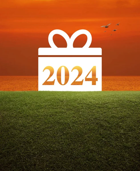 Gift box happy new year 2024 flat icon on green grass field over sunset sky and sea, Business happy new year 2024 shopping concept