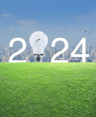 2024 beyaz metin ve içinde rüzgar türbini olan ampul modern şehir kulesi ve gökdelenin üzerindeki yeşil çimen tarlasında mutlu yeni yıl 2024 ekolojik örtüsü konsepti