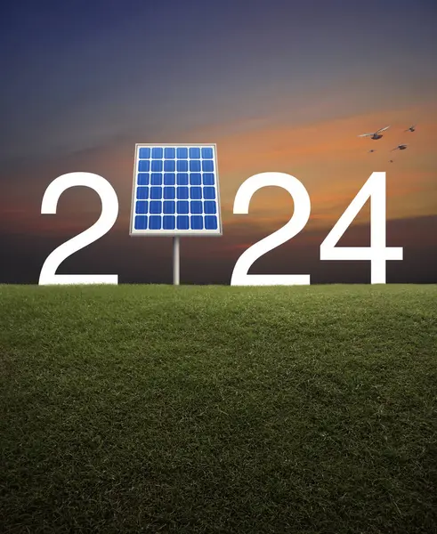 幸せな新年2024エコカバーコンセプトと夕日空の上に緑の草のフィールド上のソーラーセルを持つ2024白いテキスト ストック写真