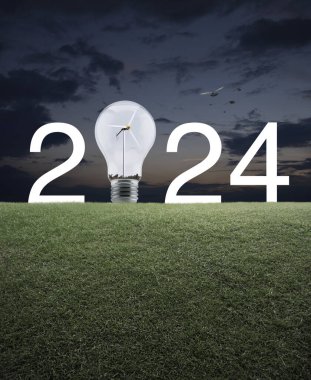 2024 beyaz yazı ve ampul içinde rüzgar türbini olan yeşil çimlerin üzerinde günbatımı gökyüzünde kuşlarla birlikte. Mutlu yıllar 2024 ekolojik kapak kavramı.