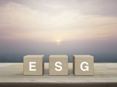 Ahşap blok küplere ESG harfi modern şehir kulesinin üzerinde ahşap masa üzerinde ve günbatımında gökdelen, klasik tarzda, Çevresel Sosyal Yönetim kavramı