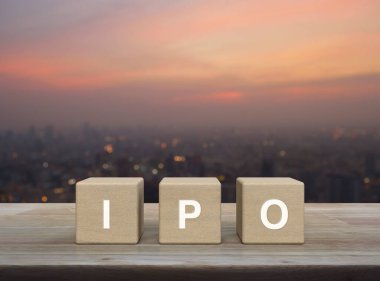 IPO letter on wood block cubes on wooden table over blur of cityscape on warm light sundown, Initial public offering concept