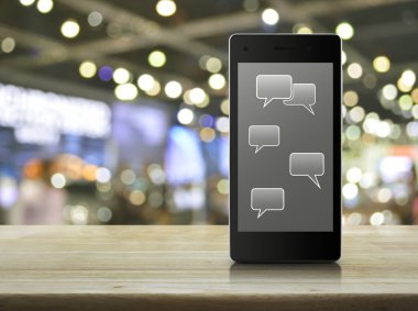 Modern akıllı cep telefonu ekranında sosyal sohbet işareti ve konuşma baloncukları. Ahşap masa üzerinde bulanık ışık ve alışveriş merkezinin gölgesi, sosyal ağ konsepti.