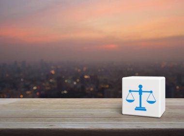 Kanun simgesi, ahşap masanın üzerindeki beyaz blok küpünde sıcak gün batımında şehir manzarası bulanıklığı, iş hukuku konsepti.