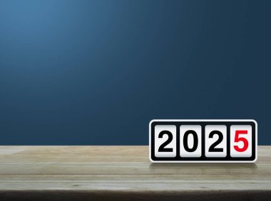 Açık mavi duvarın üzerindeki ahşap masa üzerinde 2025 metin ile ters saat, Mutlu yıllar 2025 kapak konsepti