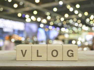 Vlog letter on wood block cubes on wooden table over blur light and shadow of shopping mall, Vlog video marketing concept