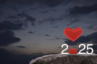 Kırmızı Kumaş Kalp, 2025 beyaz yazılı hava balonunu sever. Gün batımında gökyüzünde kaya dağında. Mutlu yıllar ve Sevgililer Günü 2025 konsepti.