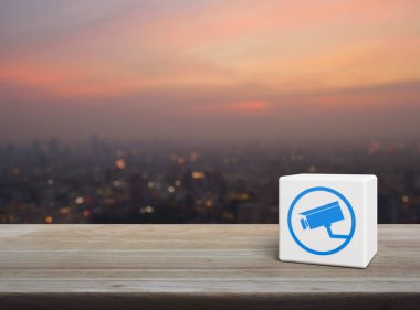 Güvenlik kamerası simgesi beyaz blok küp üzerinde ahşap masa üzerinde sıcak gün batımında şehir manzarası bulanıklığı, Teknoloji güvenliği ve güvenlik online konsepti