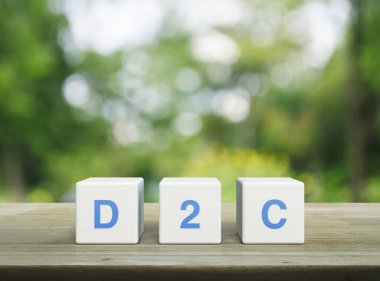 Beyaz blok küpleri üzerindeki D2C kısaltması parktaki bulanık yeşil ağacın üzerindeki ahşap masa, Tüketici Konseptine Doğrudan