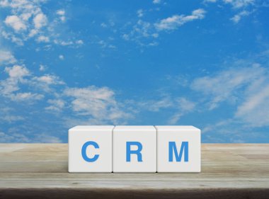 CRM kısaltması beyaz bulutlu mavi gökyüzü üzerindeki ahşap masa üzerindeki beyaz blok küpleri, Müşteri İlişkileri Yönetimi kavramı