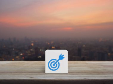 Dart düz ikonlu hedef, beyaz blok küpünün üzerinde, ahşap masanın üzerinde, şehir manzarası, sıcak gün batımında, iş başarısı konsepti.