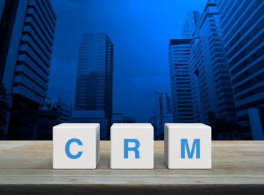 CRM kısaltması beyaz blok küpleri üzerinde ahşap masa üzerinde modern ofis kulesi ve gökdelen üzerinde, Müşteri İlişkileri Yönetimi konsepti