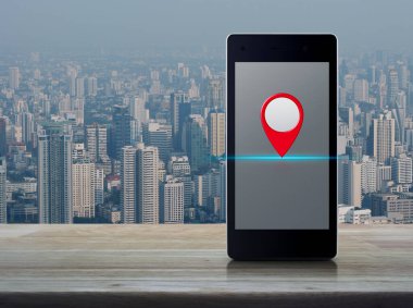 Harita pin düğmesi modern akıllı cep telefonu ekranı ahşap masa üzerinde şehir kulesi ve gökdelen, harita işaretleyici navigasyon konsepti