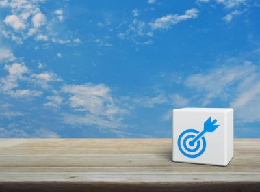 Dart düz ikonlu hedef beyaz blok küp üzerinde tahta masa üzerinde beyaz bulutlu mavi gökyüzü, iş başarısı konsepti