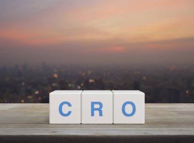 Beyaz blok küplerindeki CRO kısaltması ahşap masadaki bulanık şehir manzarasının üzerindeki sıcak gün batımındaki dönüşüm oranı optimizasyon konsepti.