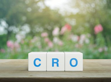 CRO kısaltması beyaz blok küpleri üzerinde ahşap masa üzerinde bulanık pembe çiçek ve bahçede ağaç, Dönüşüm Oranı İyimserleştirme konsepti