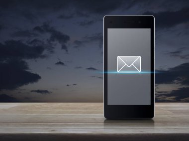 Günbatımı gökyüzü üzerinde ahşap masadaki modern akıllı cep telefonu ekranındaki e-posta düz simgesi, iş iletişimi çevrimiçi konsepti