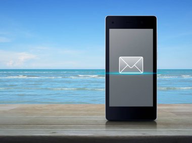 e-posta düz ahşap masa ile beyaz bulutlar, online iletişim iş kavramı mavi gökyüzü üzerinde modern akıllı cep telefonu ekran simgesine