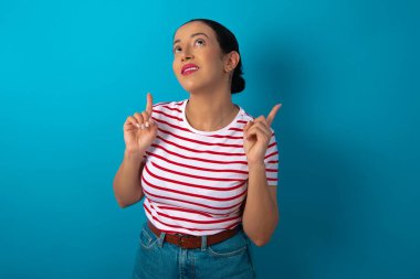 Başarılı, dost canlısı görünümlü, çizgili tişört giyen, heyecanlı bir şekilde bağıran, her iki işaret parmağıyla işaret eden bir şey gösteren bir kadın..