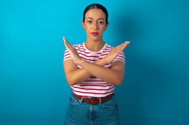 Çizgili tişört giyen bir kadın yüzünde kızgın bir ifadeyi reddediyor ve ellerini çapraz yapıyor. Negatif işareti yapıyor..