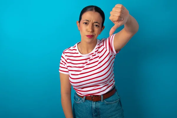 ストライプTシャツを着用している不満の女性は 不承認のサインを示し 親指を保ち 不満で嫌い 凍った顔を表現します ネガティブな感情 — ストック写真