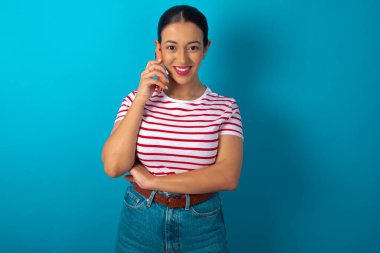 Çizgili tişört giyen, cep telefonuyla konuşan gülümseyen bir kadının portresi. İş, güven ve iletişim kavramı.