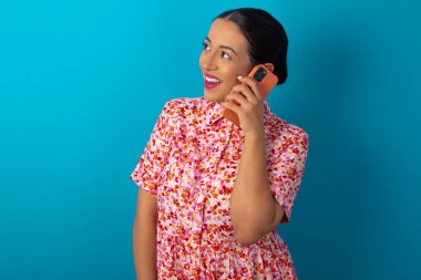 Çiçekli elbise giyen mutlu bir kadın güzel bir telefon görüşmesi yapar ve yan gelip bakar, cep telefonuyla konuşurken güzel bir havası vardır ve gülümser.