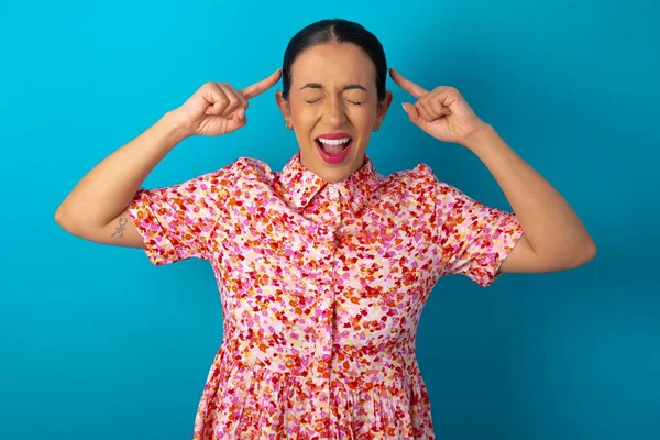 Photo of crazy woman wearing floral dress over blue studio background screaming and pointing with fingers at hair closed eyes