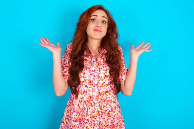 Belki evet ya da hayır. Mavi arka planda çiçekli elbise giyen kızıl saçlı şüpheli bir kadın şaşkınlıkla omuz silkiyor, ne istediğine karar vermeye çalışıyor. Tereddüt ve belirsizlik.