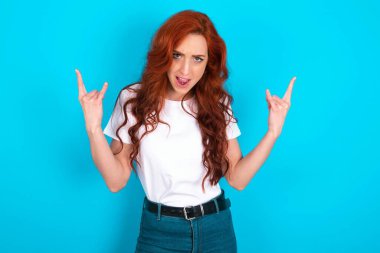 Bu dünyayı sallamak için doğmuşum. Mavi arka planda beyaz tişört giyen neşeli kızıl kadın yüksek sesle bağırıyor ve kollarını kaldırarak ya da taş gibi hareketlerle gösteriyor..