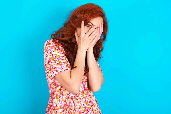 Redhead Woman Wearing Floral Dress Blue Background Covering Face Hands — Stock Photo, Image