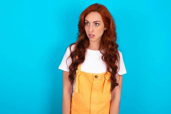 Redhead Woman Wearing Orange Overall Blue Background Stares Aside Wondered — Stock Photo, Image