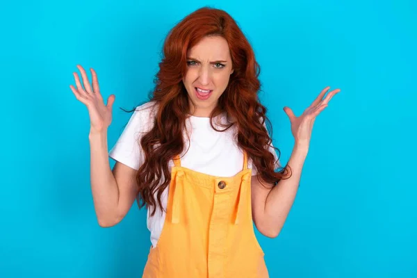 Crazy Outraged Redhead Woman Wearing Orange Overall Blue Background Screams — Stock Photo, Image