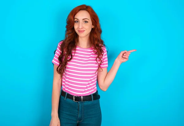 在蓝色背景下穿着粉色条纹T恤 表情满意的红头发女人表示 在右上角有很好的选择 建议点击链接 — 图库照片