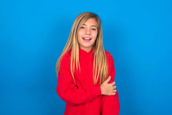青い背景に笑う青い背景の上に赤いスウェットシャツを着ている笑顔の慎重な十代の少女 — ストック写真