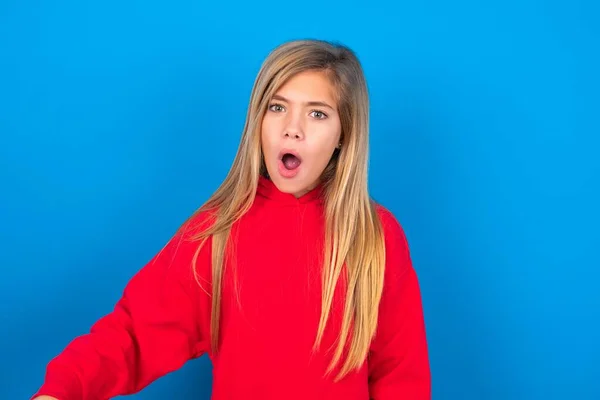 Zszokowany Oszołomiony Biały Nastolatek Dziewczyna Czerwonej Bluzie Niebieskim Tle Utrzymuje — Zdjęcie stockowe