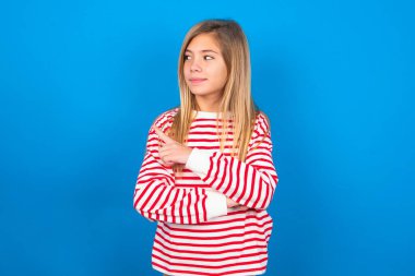 Mavi arka planda çizgili tişört giyen genç kızın portresi. Kamera önünde hileli bir bakışla poz veriyor. Ürünü işaret parmağıyla sunuyor. Reklam kavramı.