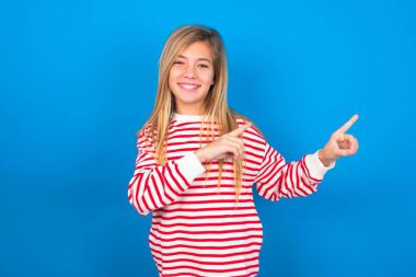 Mavi arka planda çizgili tişört giyen, gülümseyen, iki parmağıyla işaret eden ve boş fotokopi odasına bakan pozitif bir genç kız. Reklam kavramı.